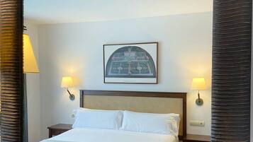 Habitación de hotel con un espejo grande, una cama con sábanas blancas, dos lámparas de noche y un cuadro en la pared.