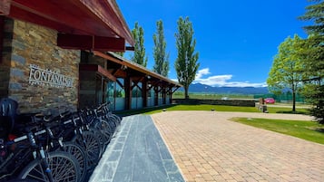 Entrada de hotel com fachada de pedra, área de estar coberta ao ar livre e bicicletas estacionadas.