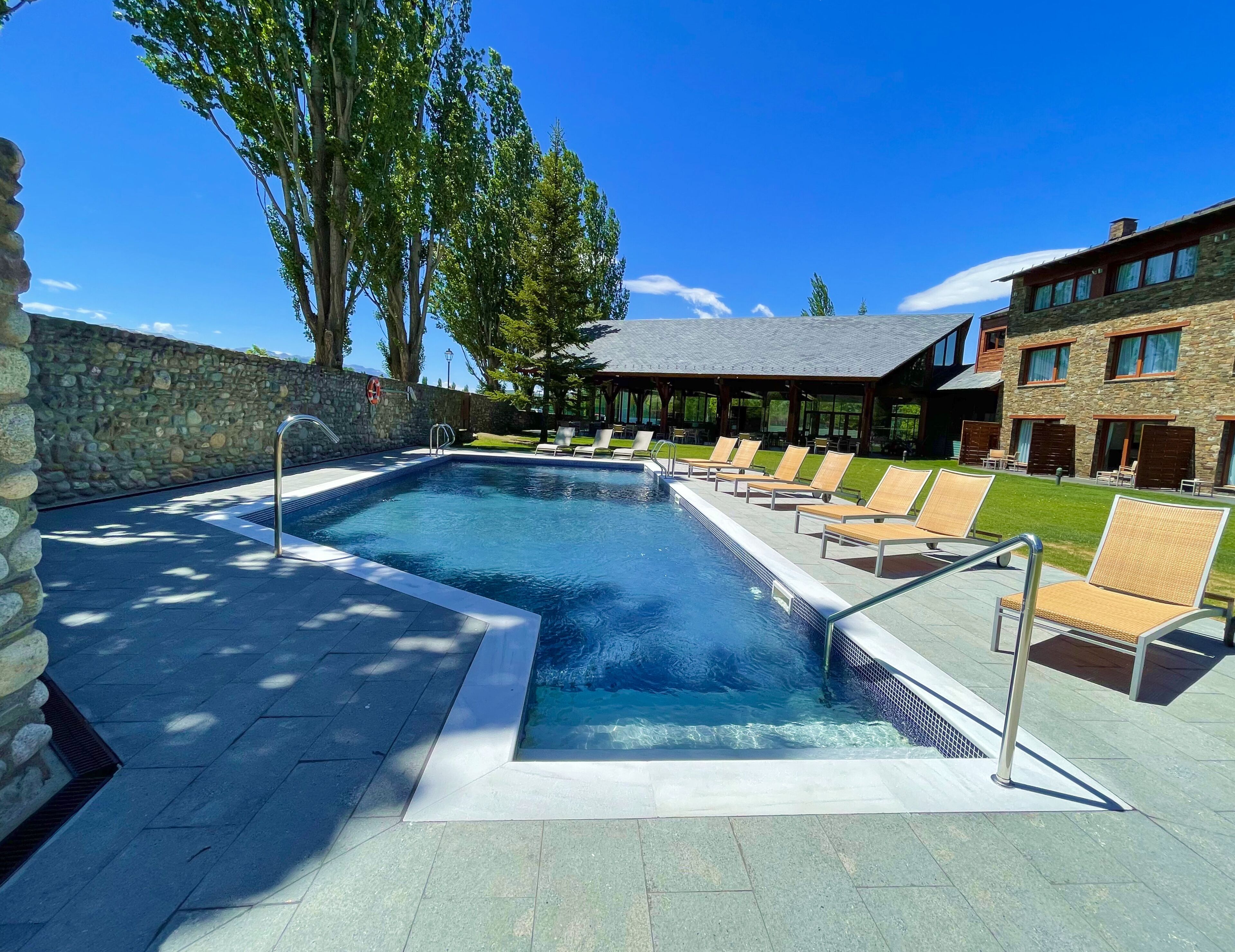 Una piscina amb gandules, una paret de pedra i un edifici amb grans finestres.