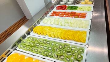 Un bufé con diversas frutas y verduras dispuestas ordenadamente en bandejas.