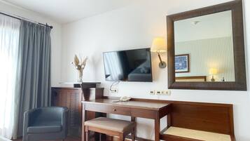 Una habitación de hotel con un escritorio de madera, una silla, un televisor, un espejo y una lámpara.
