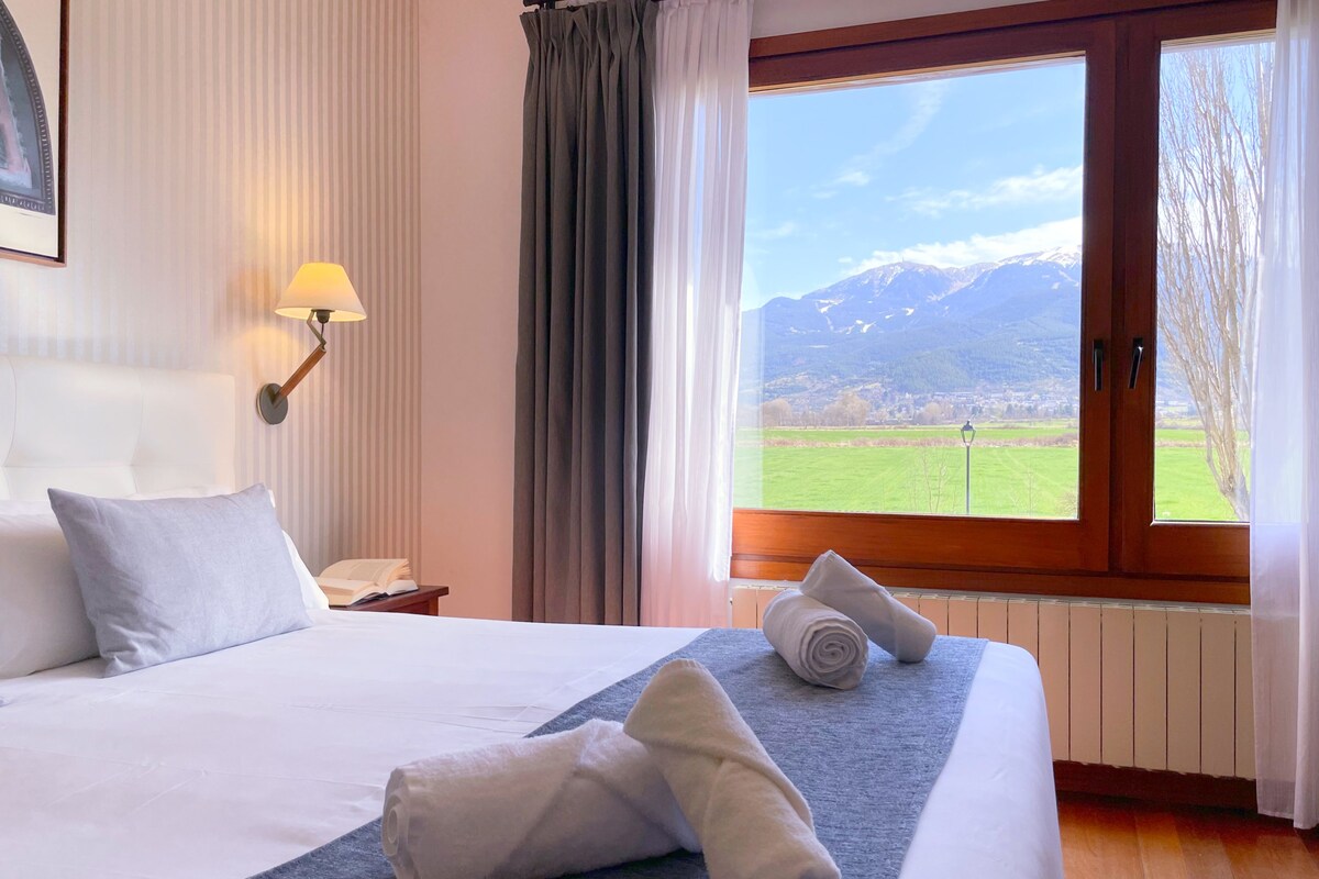 A hotel room with a large bed, a view of mountains, and a window with curtains.