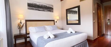Habitación de hotel con una cama grande, dos mesitas de noche, un espejo y un cuadro en la pared.
