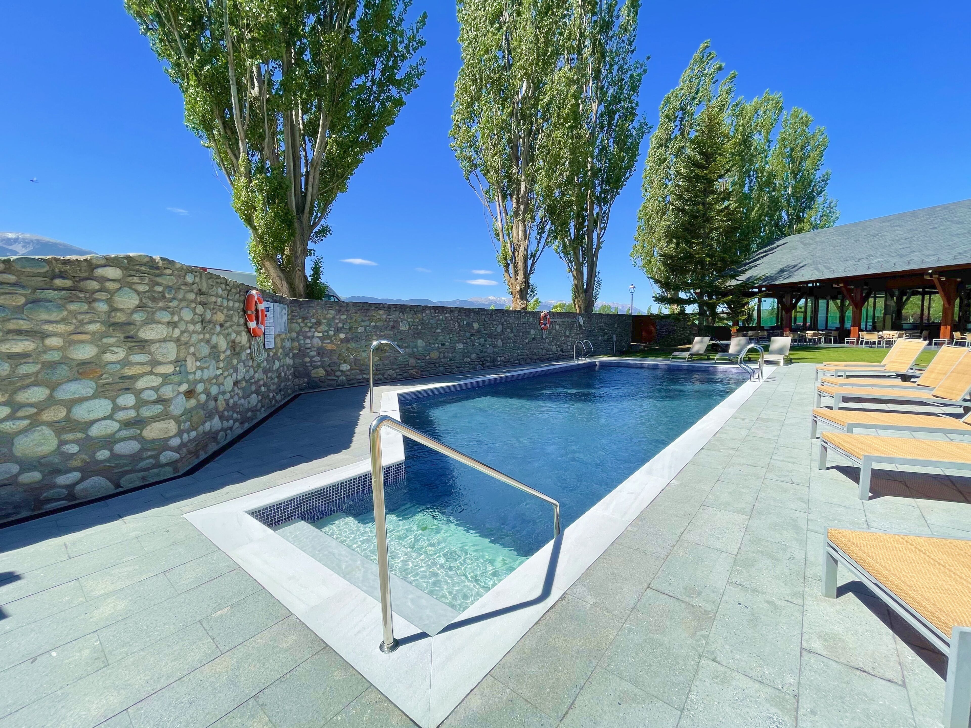 Une piscine avec des murs en pierre, des chaises longues et un espace abrité.