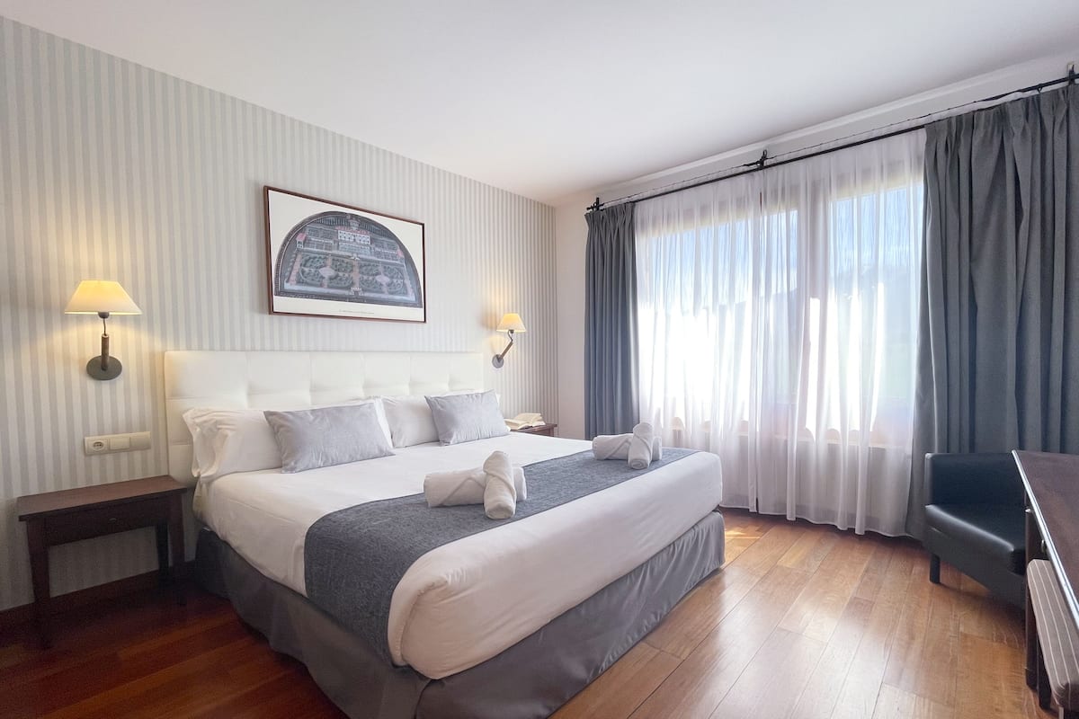 Une chambre d’hôtel avec un grand lit, deux tables de chevet, un bureau et une fenêtre avec des rideaux.