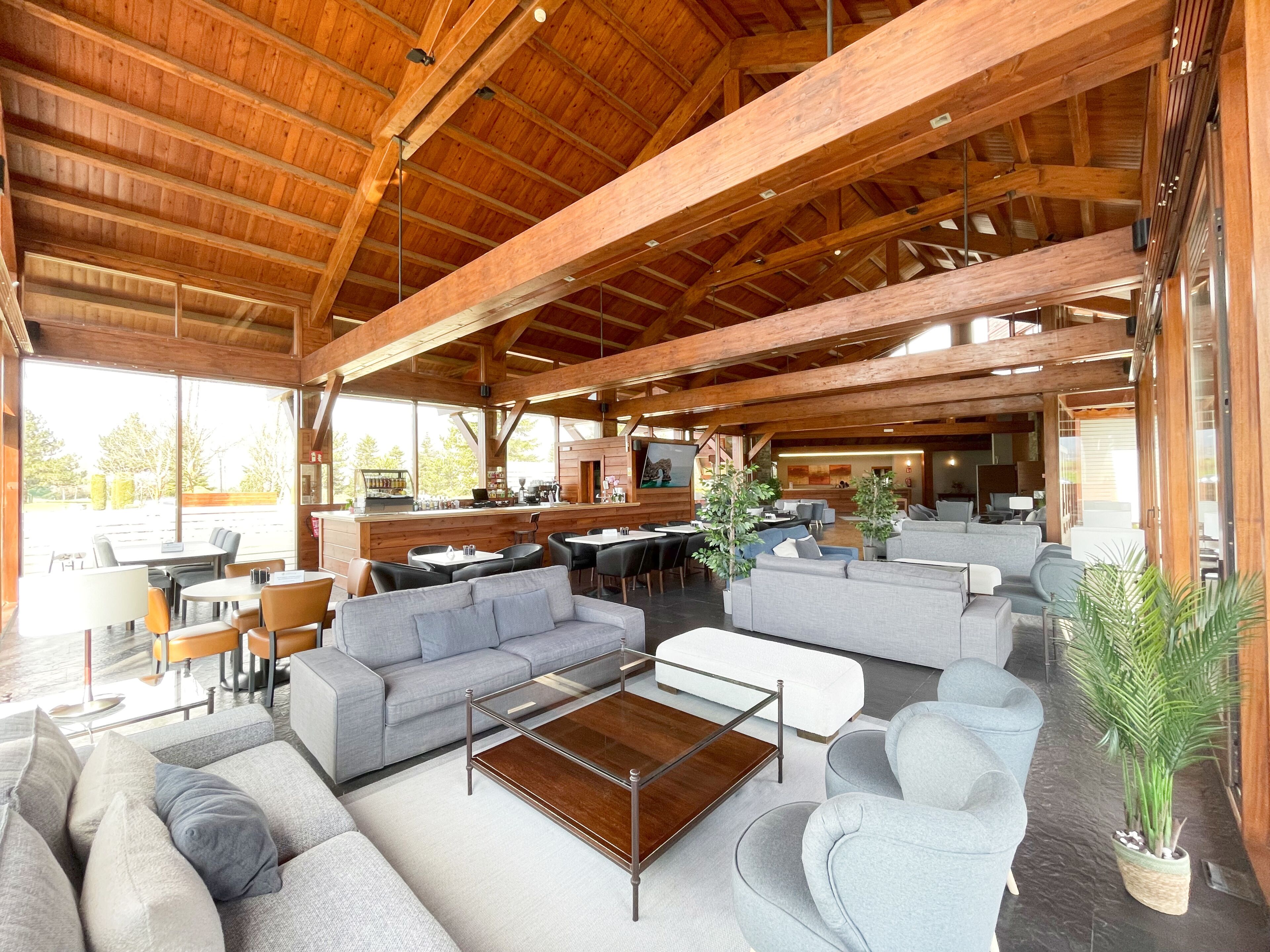 A spacious indoor area with wooden beams, seating arrangements, and a bar area.