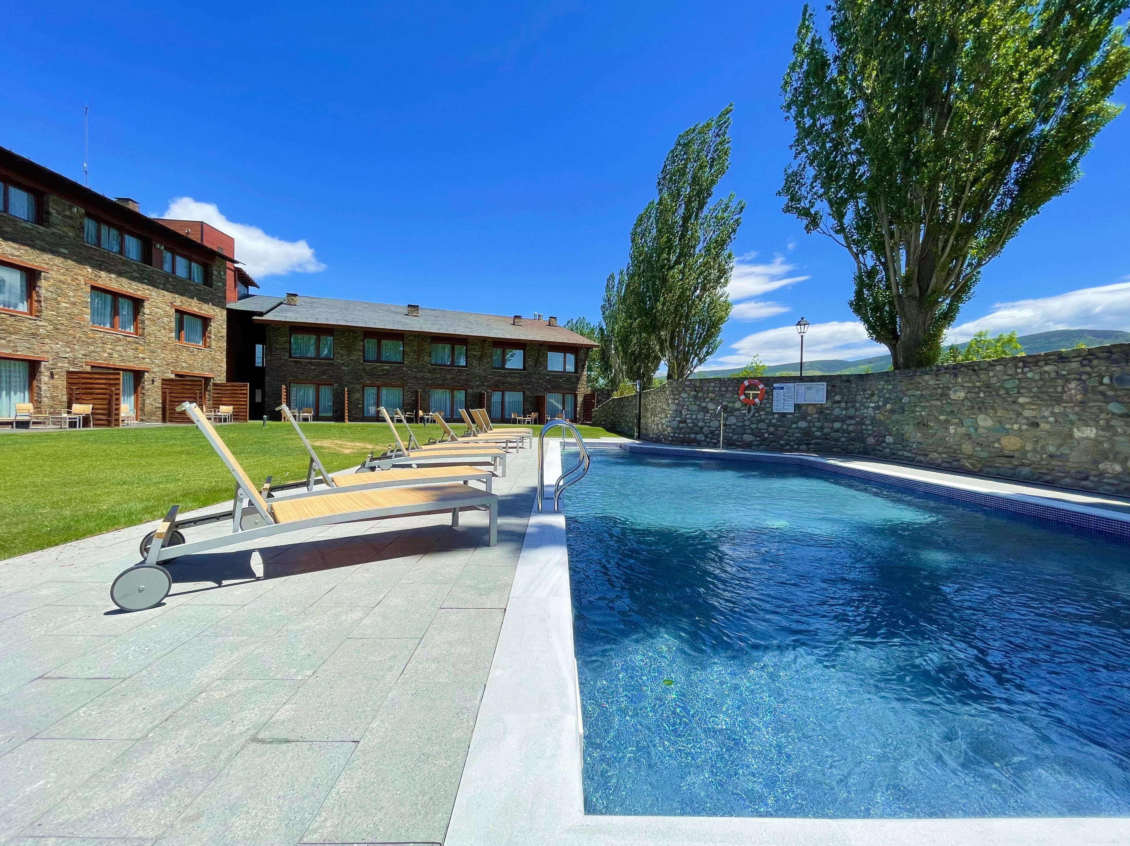 Una piscina con sillas de descanso, un muro de piedra y un edificio con varias ventanas.