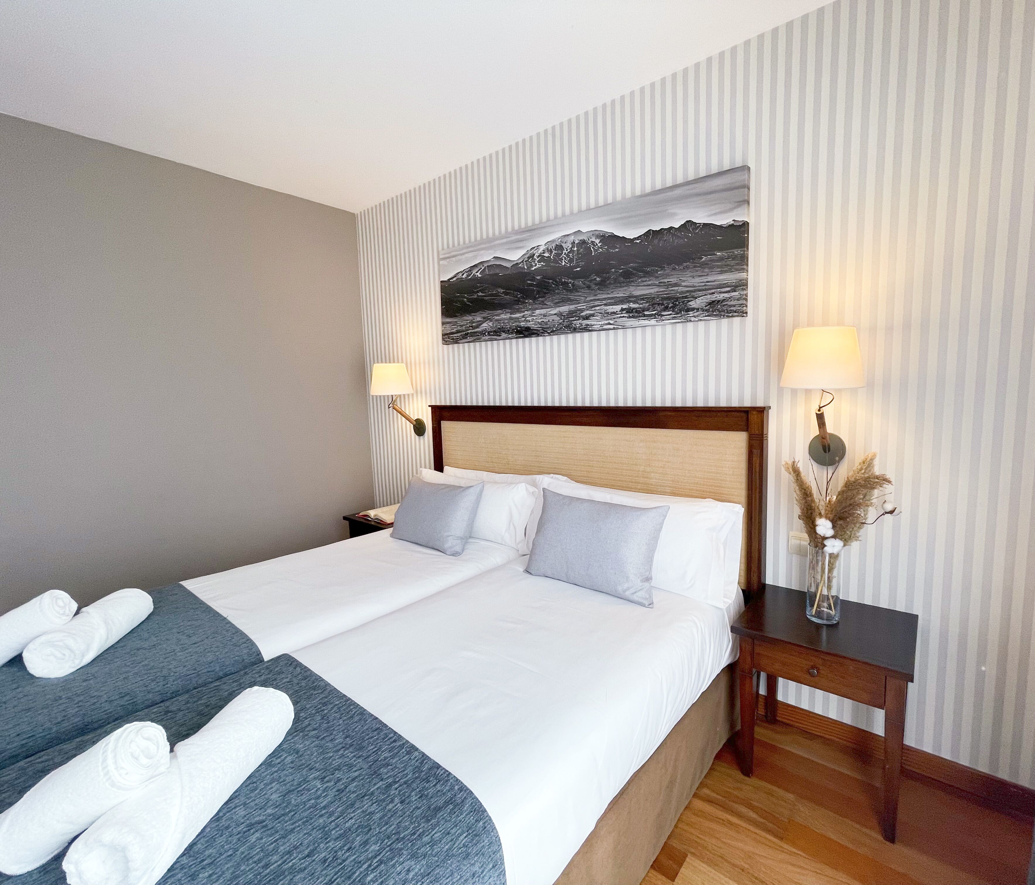 A hotel room with a large bed, two bedside tables, a nightstand, a wall-mounted lamp, and a framed picture above the bed.