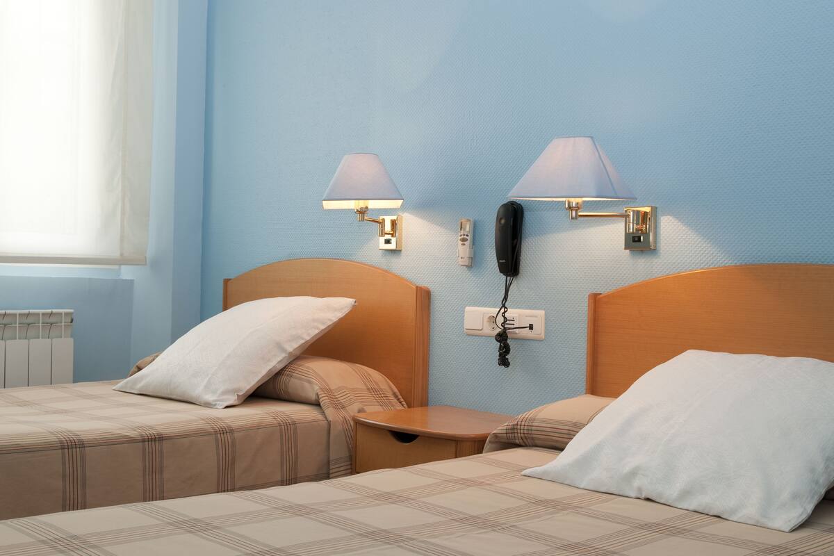 A hotel room with two beds, a nightstand, a telephone, and wall-mounted lamps.