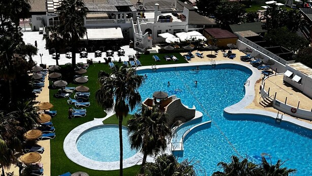 A resort with a large swimming pool, beach area, and palm trees.
