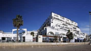 A multi-story hotel with balconies, a beachside location, and a clear blue sky.