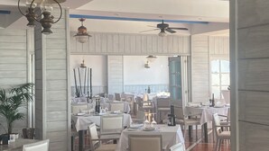 A restaurant with multiple tables and chairs, ceiling fans, and hanging light fixtures.