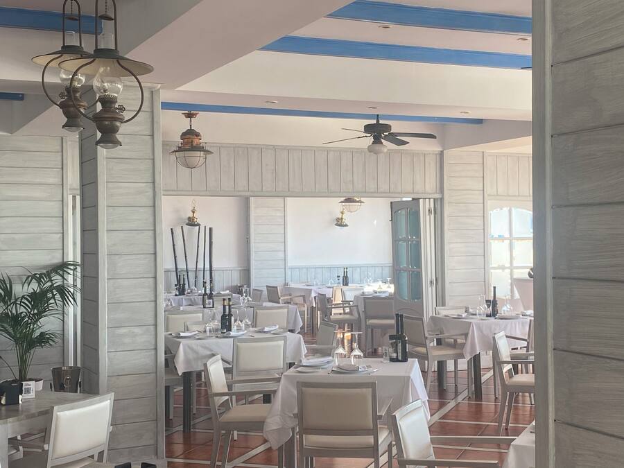 Een restaurant met meerdere tafels en stoelen, plafondventilatoren en hangende lampen.