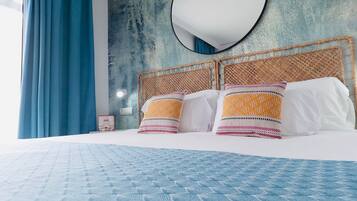 Una cama con colcha azul estampada, un espejo redondo encima y una pared texturizada al fondo.
