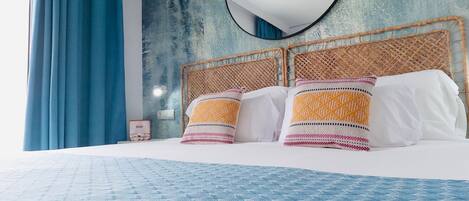 A bed with a blue patterned bedspread, a round mirror above it, and a textured wall behind.