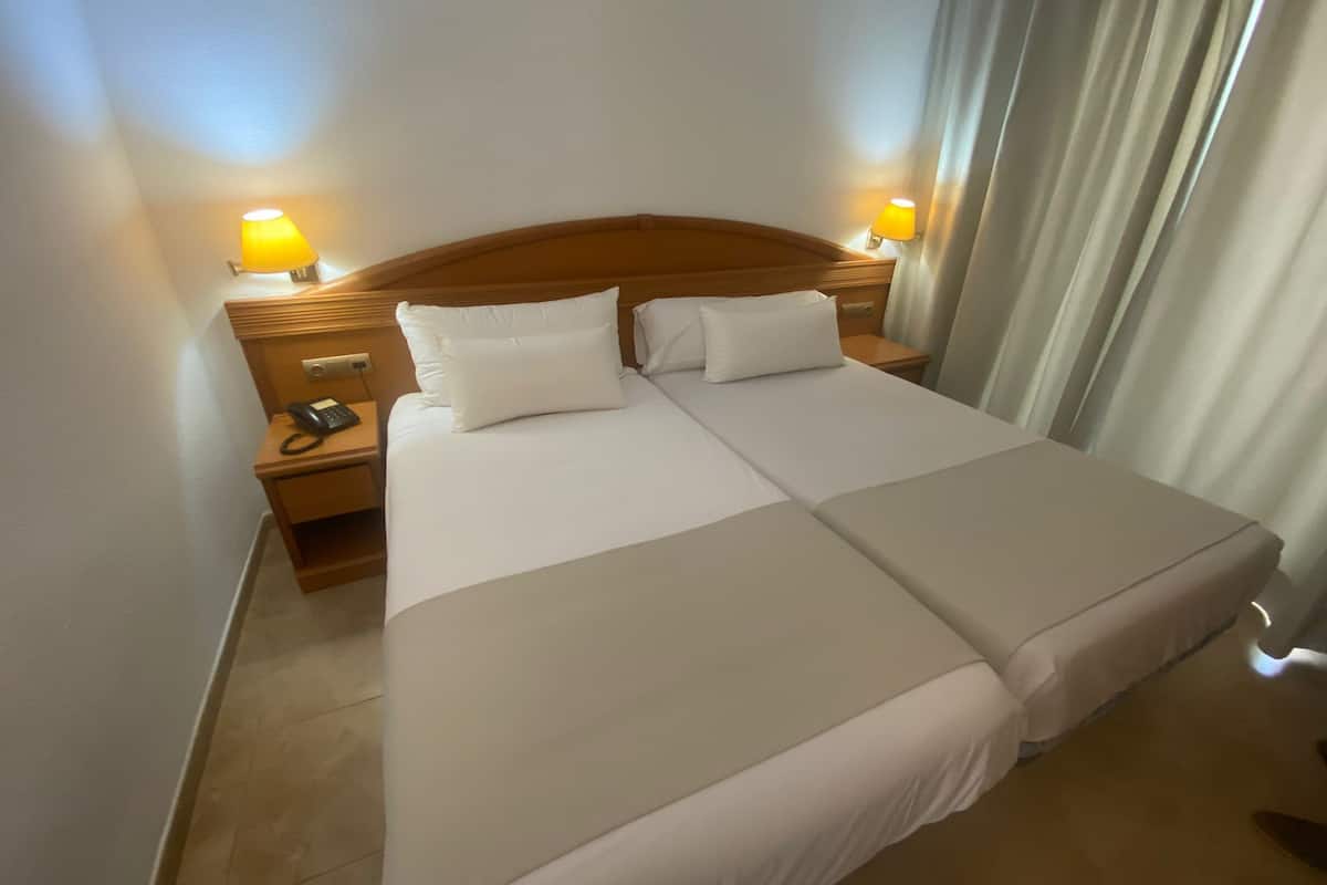 A double bed with white linens, two bedside lamps, and a wooden headboard.