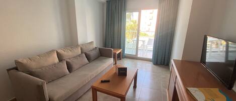 Una sala de estar con sofá, mesa de centro, televisión y puerta corrediza que da al exterior.