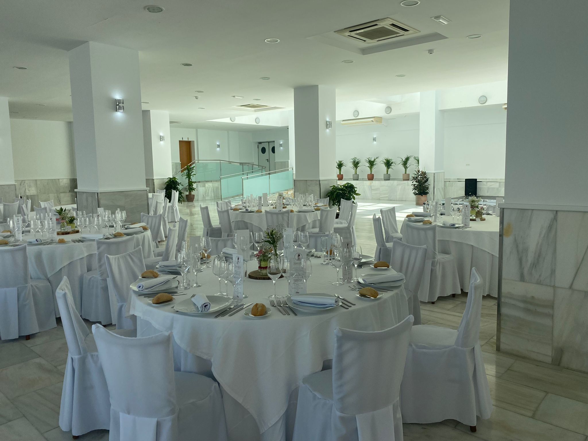 Un salón de banquetes con mesas redondas dispuestas para cenar, manteles blancos y sillas con fundas blancas.