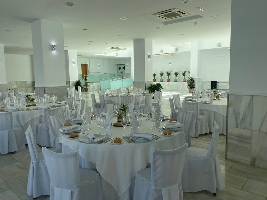 A banquet hall with round tables set for dining, white tablecloths, and chairs with white covers.