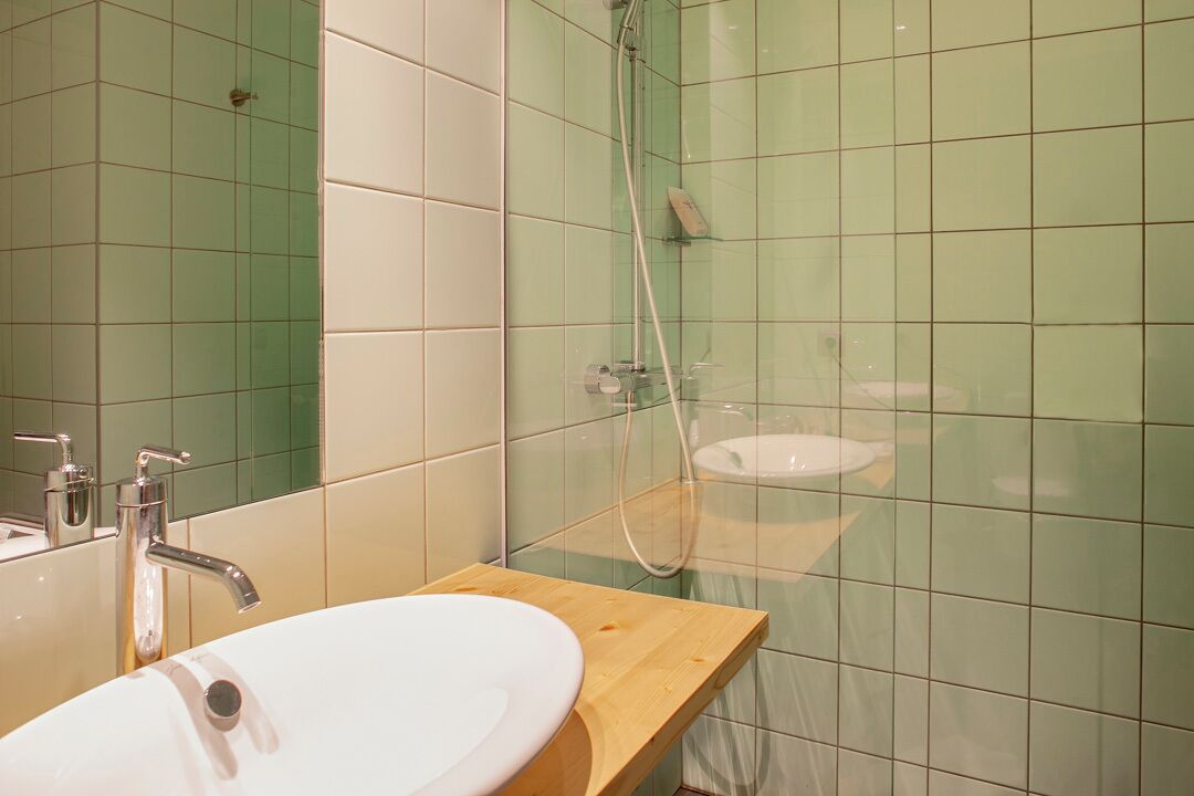 Un baño con tocador de madera, lavamanos blanco y mampara de ducha de vidrio.