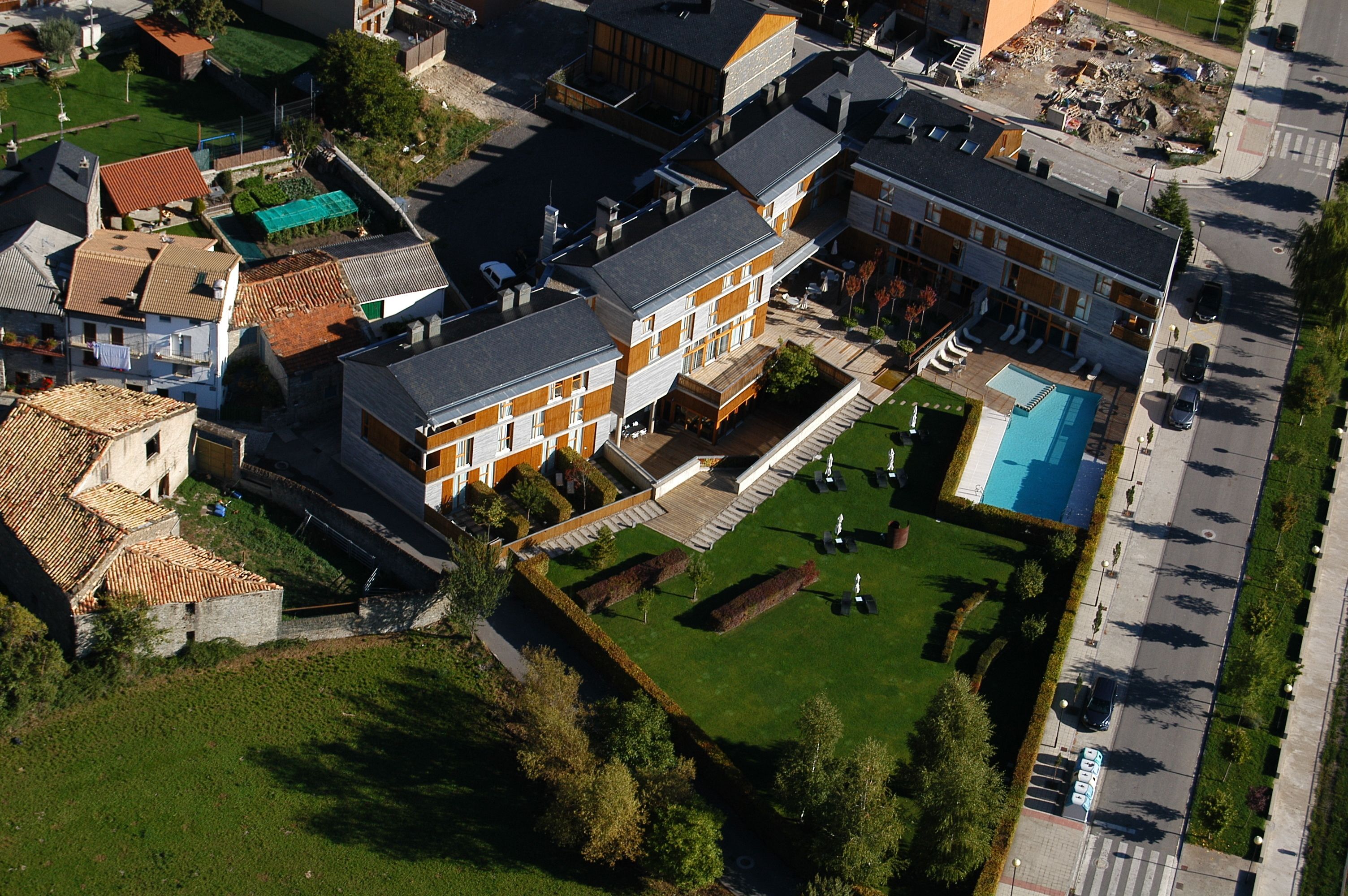 An aerial view of a residential area with a large house featuring a swimming pool, multiple balconies, and a well-maintained lawn.