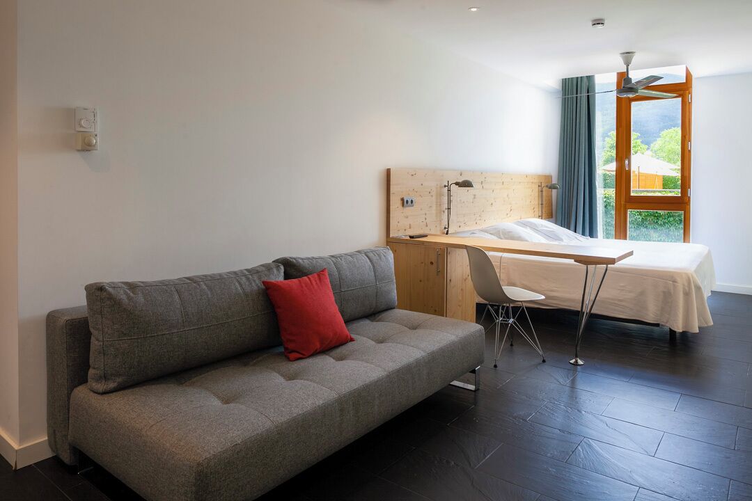 A modern room with a grey sofa, a wooden desk, and a bed.