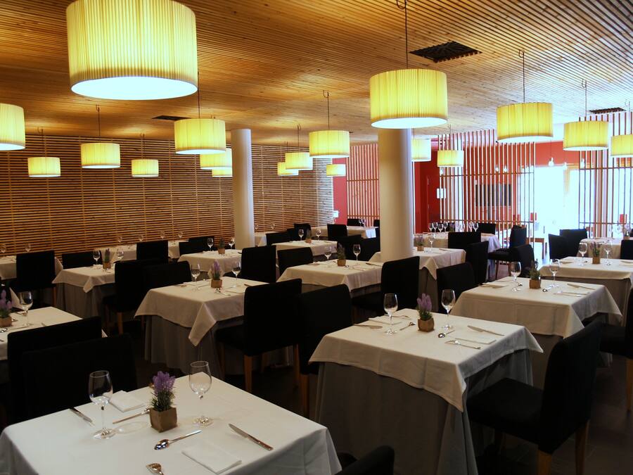A restaurant with multiple tables set for dining, featuring a wooden ceiling and yellow pendant lighting.