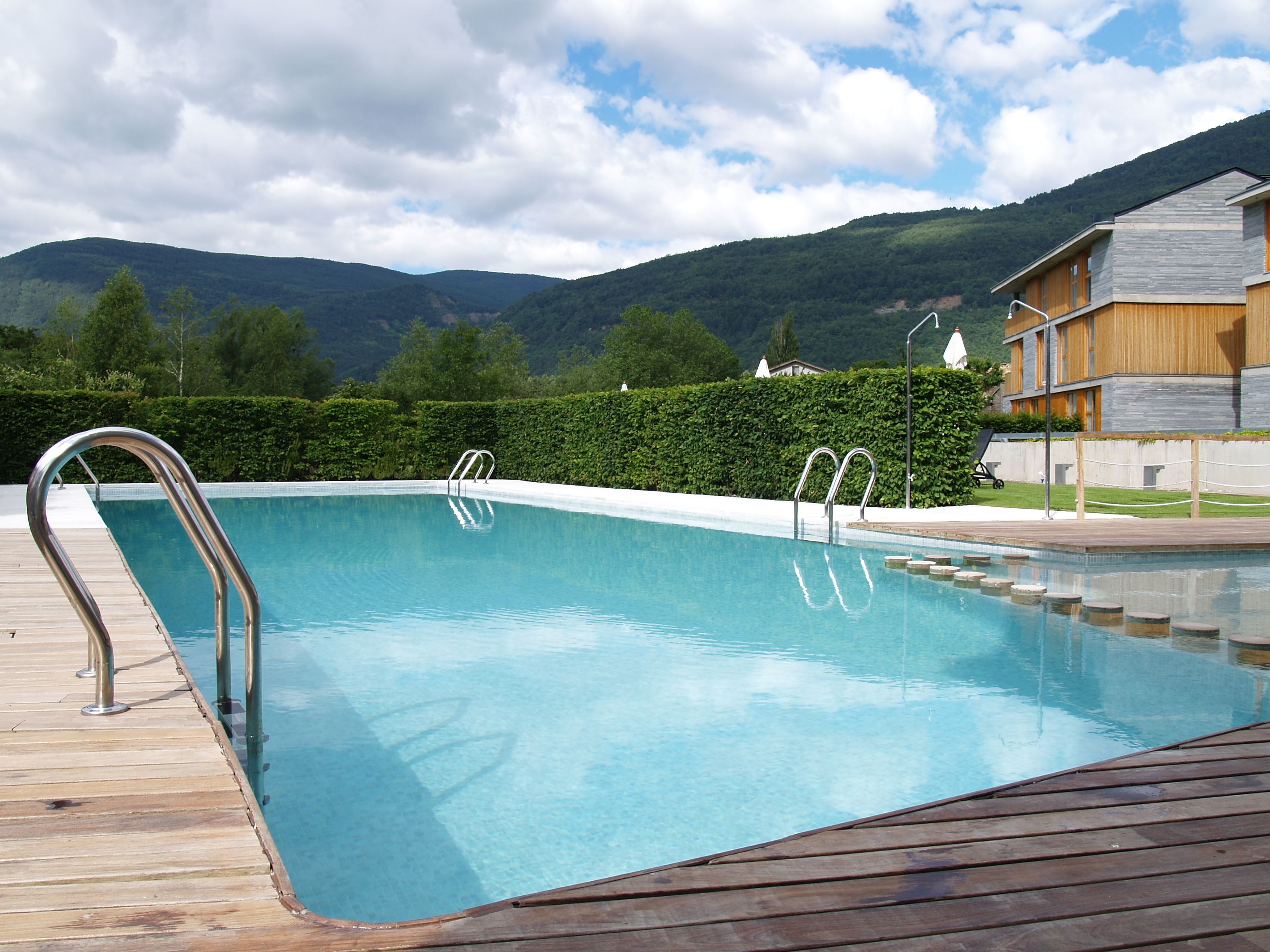Une piscine entourée de rampes métalliques, avec une terrasse en bois et une vue sur les montagnes en arrière-plan.