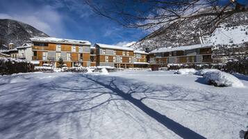 Un hotel cubierto de nieve con varias edificaciones, cielo despejado y montañas al fondo.