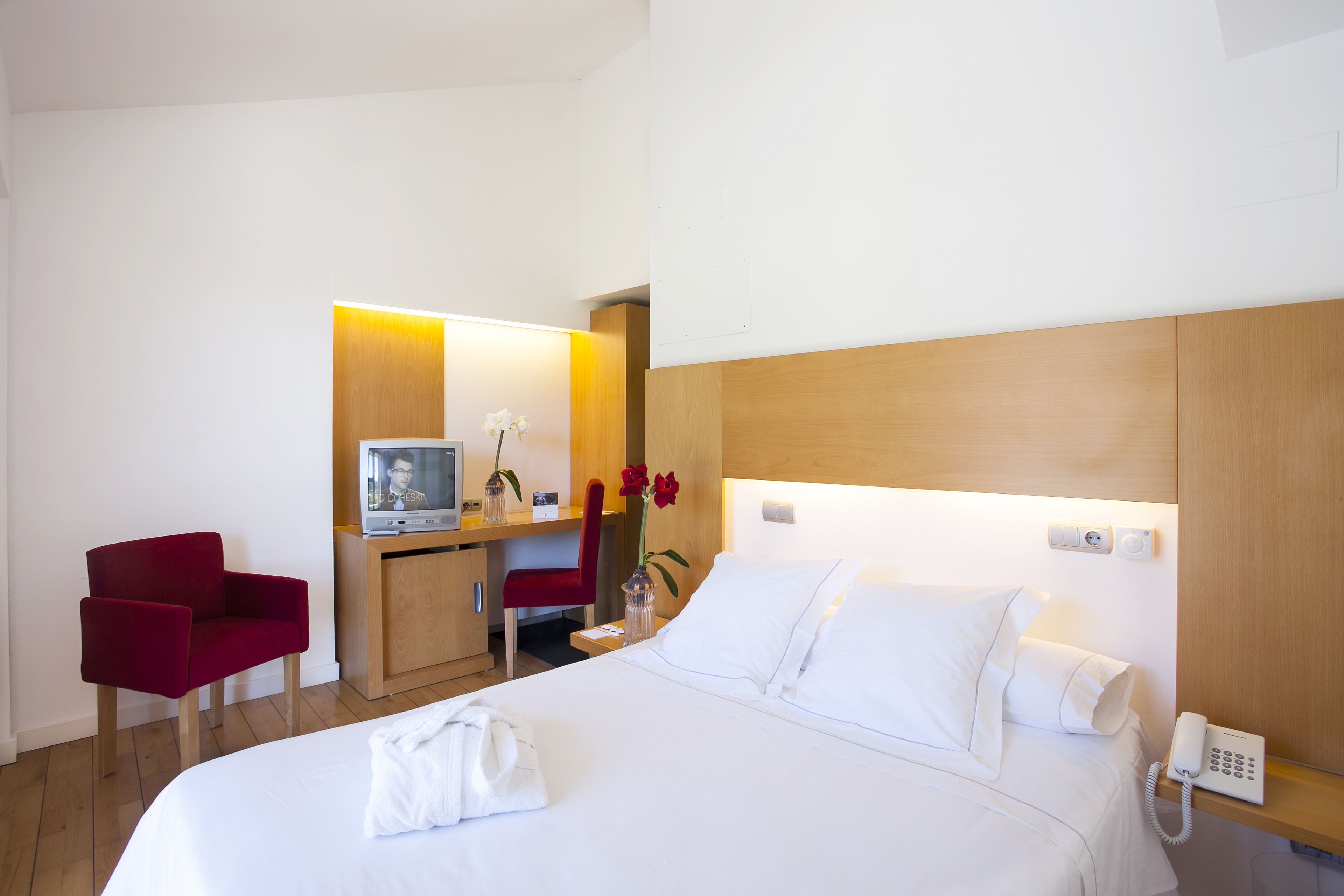 Una habitación de hotel con una cama, un escritorio con ordenador, una silla roja y un teléfono.