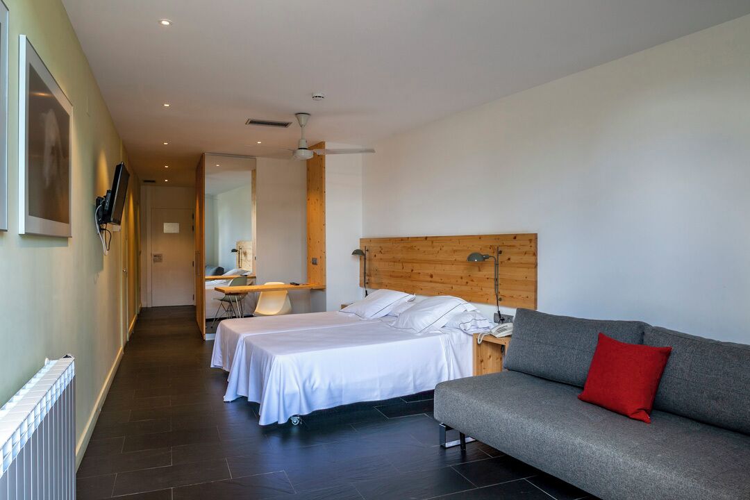 Een hotelkamer met twee bedden, een grijze bank, een houten hoofdbord en een rood kussen.