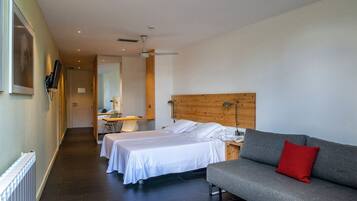 Een hotelkamer met twee bedden, een grijze bank, een houten hoofdbord en een rood kussen.