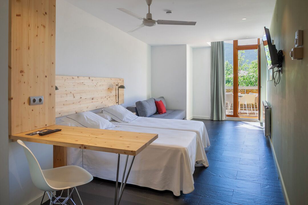 Een moderne hotelkamer met twee bedden, een houten bureau, een witte stoel en een plafondventilator.