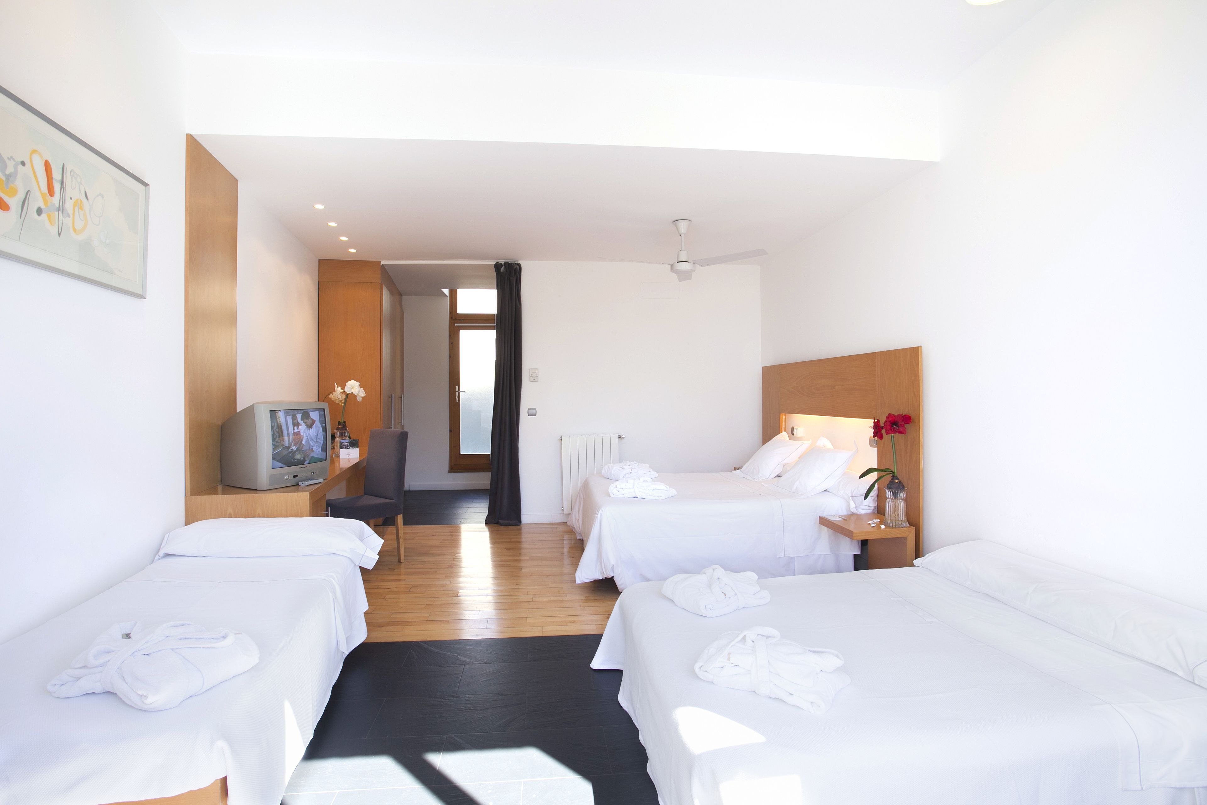 A hotel room with two beds, a TV, a desk, and a view of the hallway.