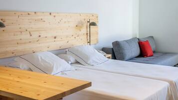 Habitación de hotel con dos camas, cabecero de madera, sofá gris con almohadones rojos y una mesa de madera.