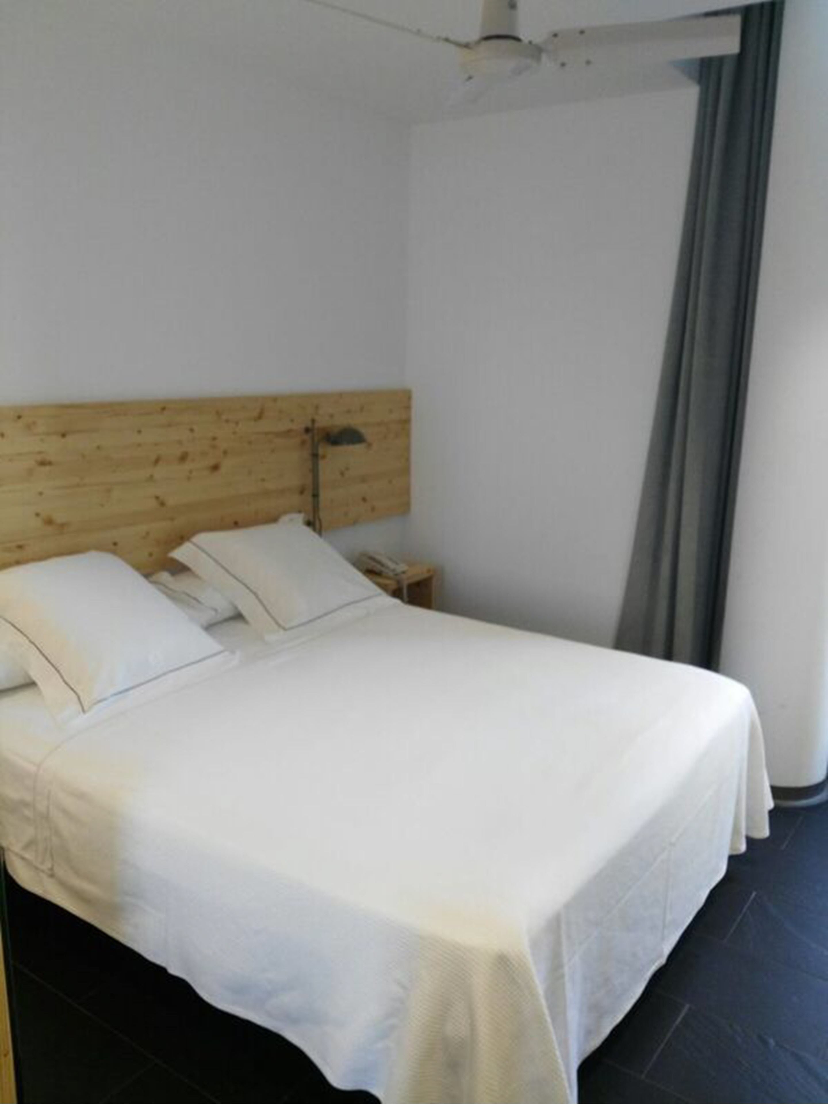 Een enkel bed met een houten hoofdeinde, witte beddengoed en een nachtkastje met een lamp.