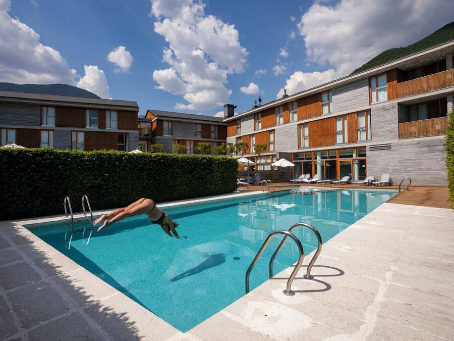 Una piscina con alguien saltando, rodeada por un edificio moderno con balcones y un cielo despejado.