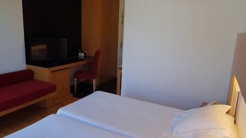 A hotel room with a bed, a desk, a chair, and a television.