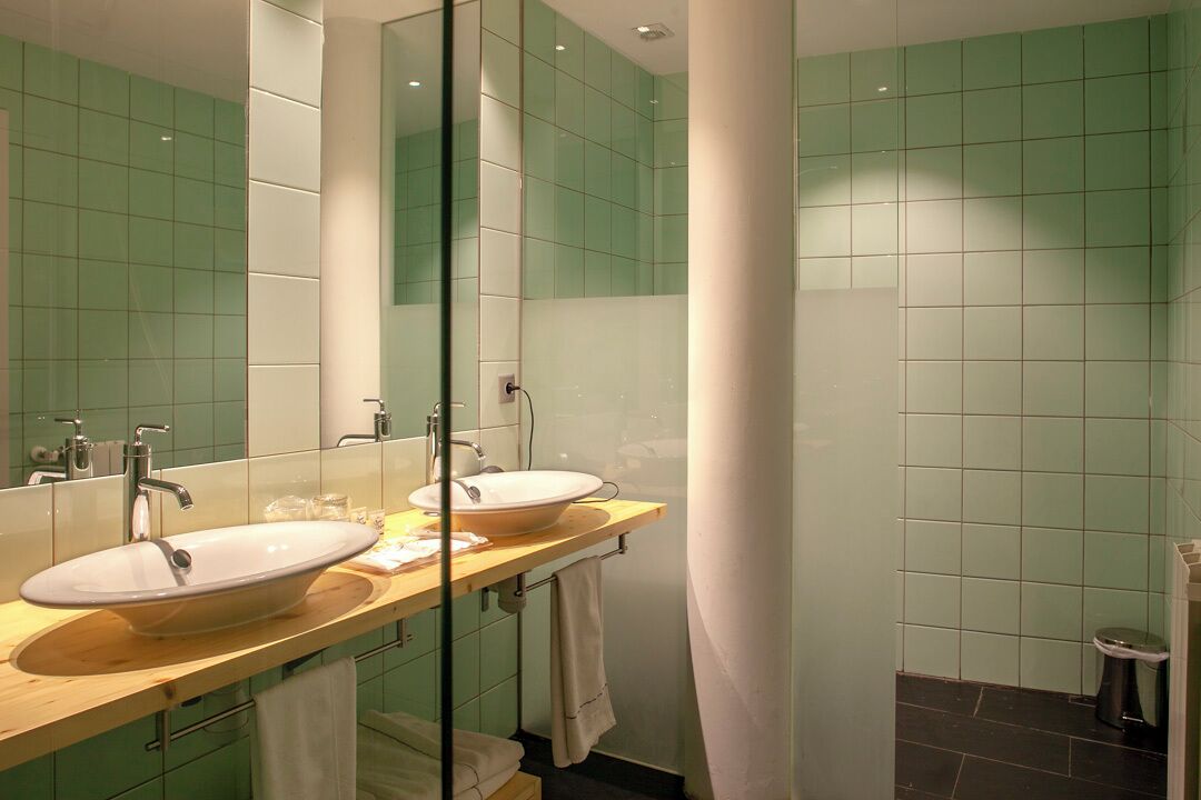 Un baño moderno con dos lavamanos, un espejo grande y paredes con azulejos verdes.
