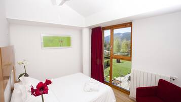 A bedroom with a bed, a red chair, a window with a view of a garden and mountains, and a ceiling fan.