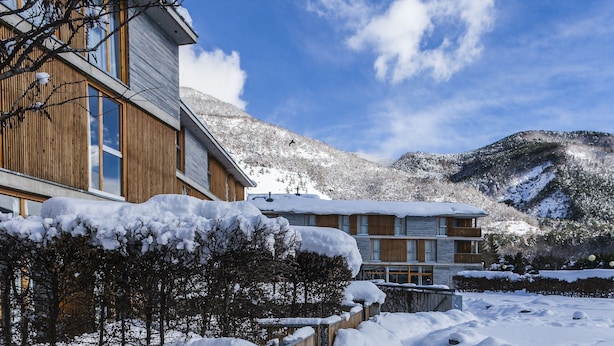 A modern building with large windows and a wooden facade, surrounded by snow-covered trees and mountains. - Tierra De Biescas Hotel (Biescas)