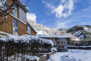 A modern building with large windows and a wooden facade, surrounded by snow-covered trees and mountains. - Tierra De Biescas Hotel (Biescas)