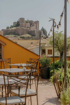 Una terraza con mesas y sillas, vista a un castillo histórico y una farola.