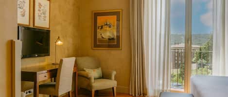 Quarto de hotel com escrivaninha, cadeira, televisão, cama e vista para o exterior.