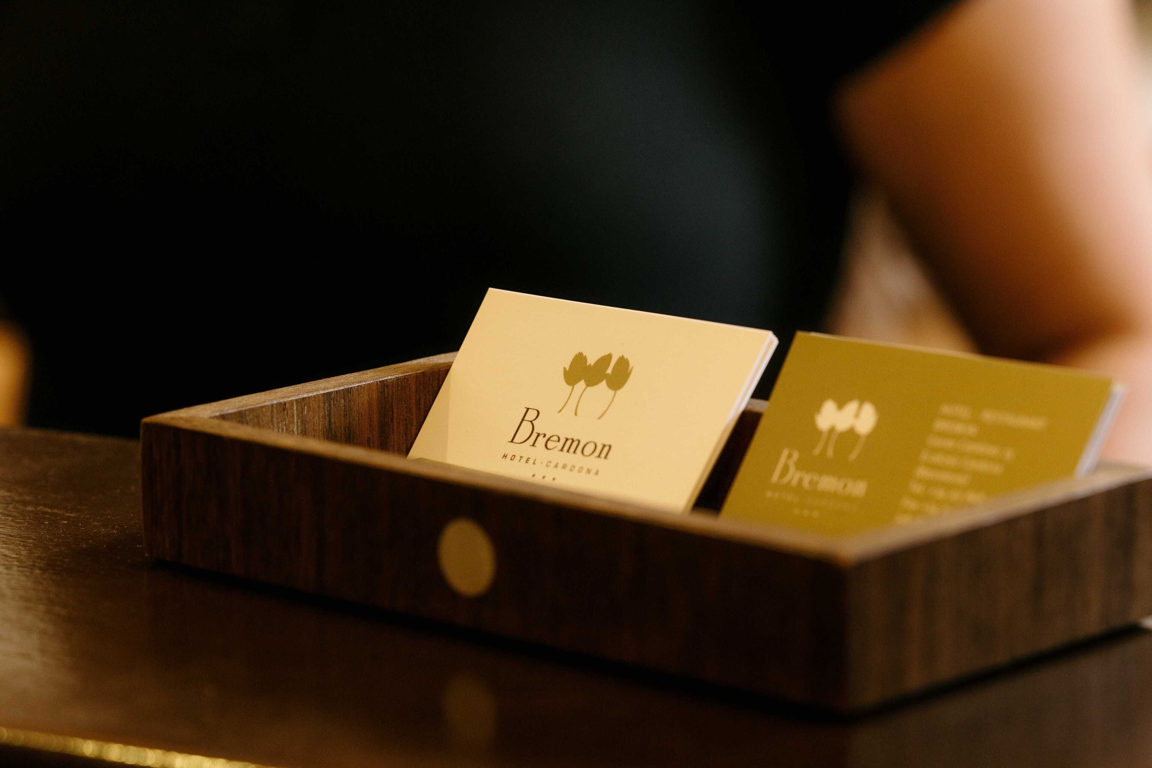 A wooden card holder with two business cards, one labeled 'Bremon HOTEL' and the other with a logo and text.