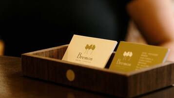 A wooden card holder with two business cards, one labeled 'Bremon HOTEL' and the other with a logo and text.