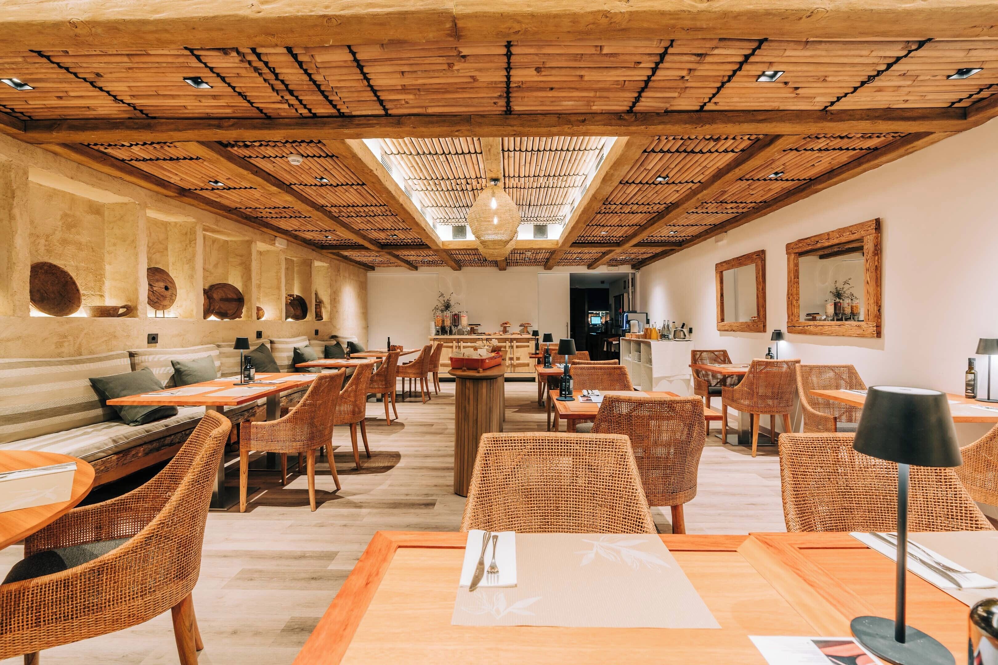 A restaurant with wooden ceiling beams, wicker furniture, and a central bar area.