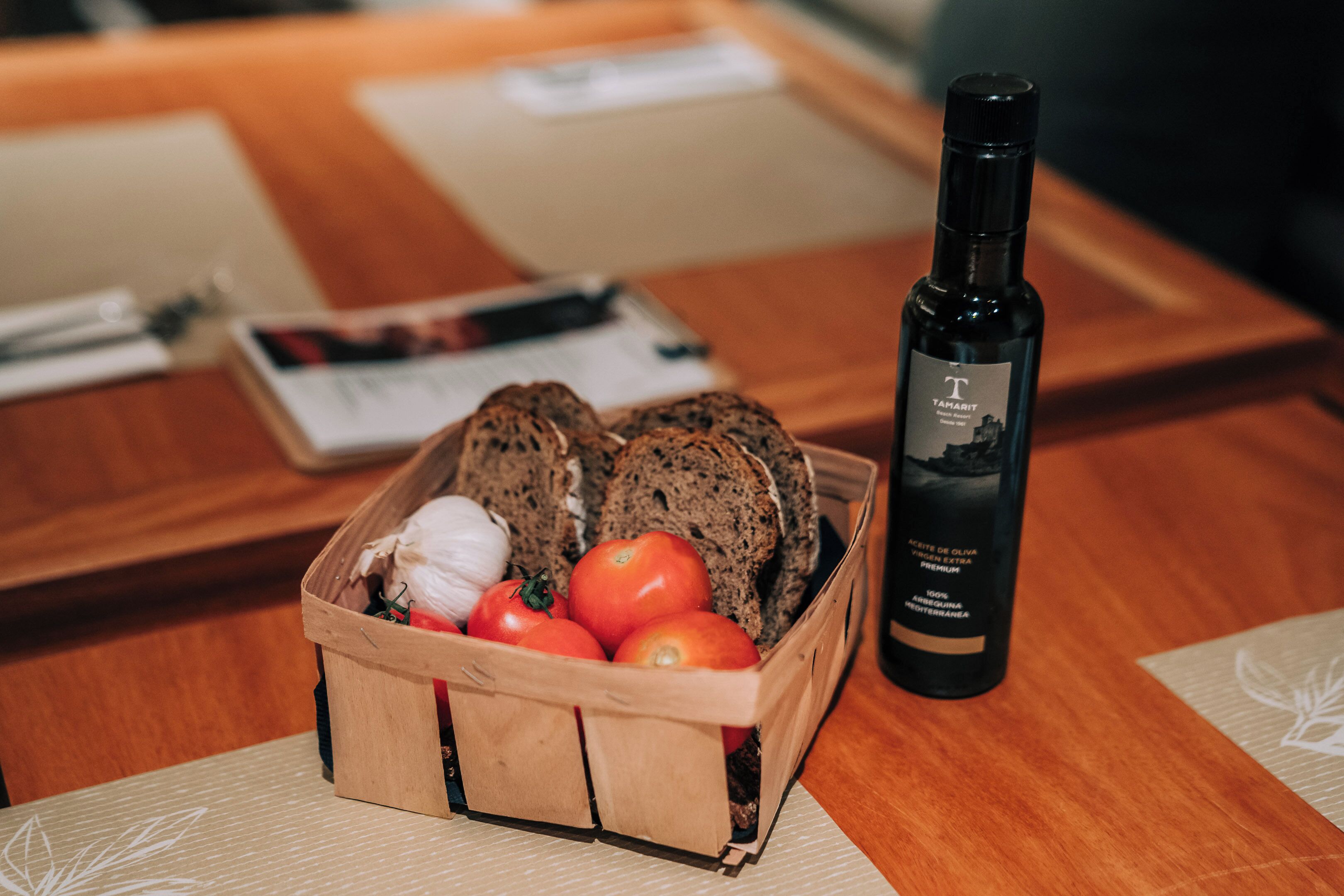 A wooden crate with bread, tomatoes, and garlic on a table.