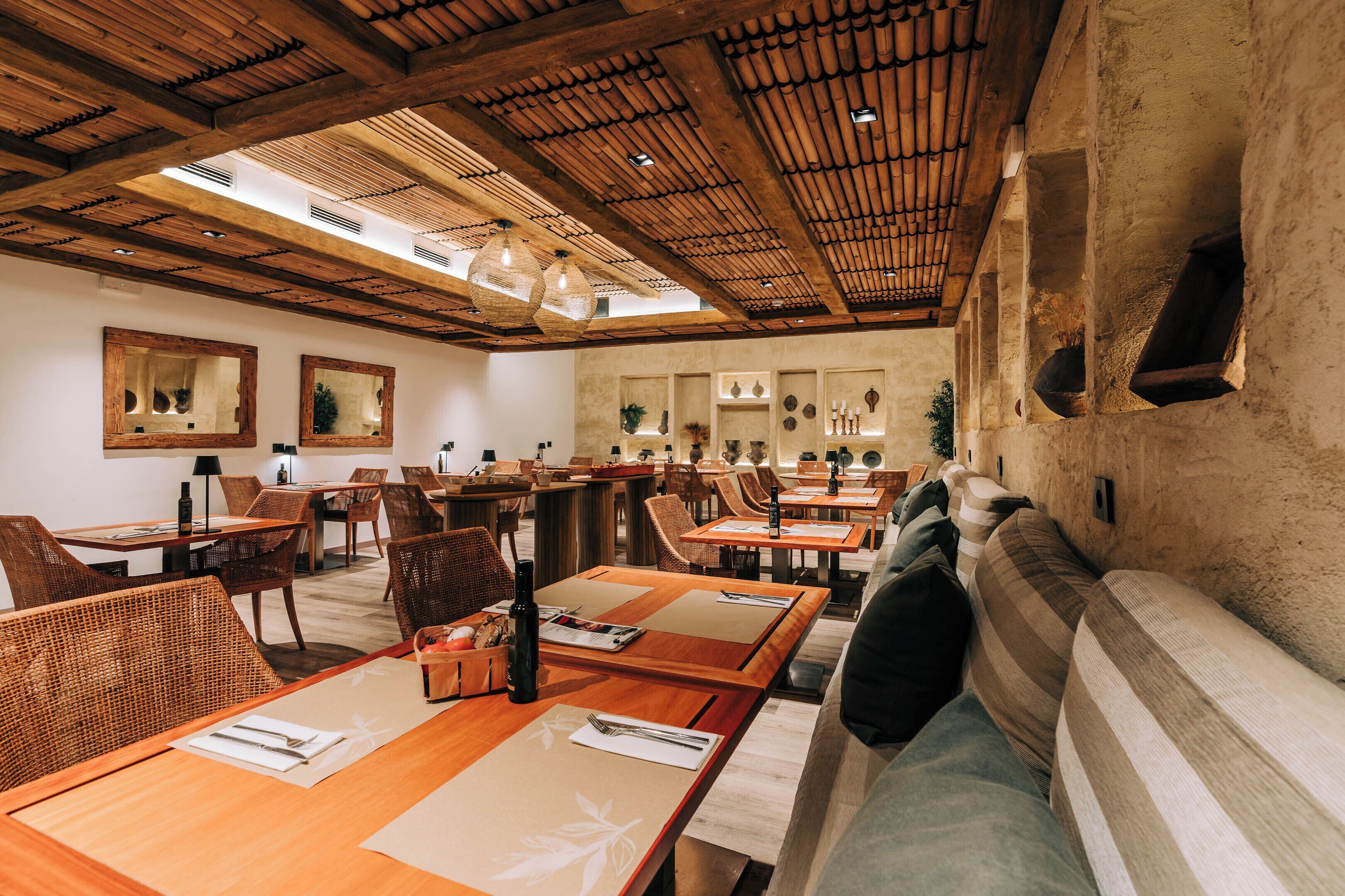 A restaurant with wooden tables and chairs, a sofa, and a high wooden ceiling with skylights.