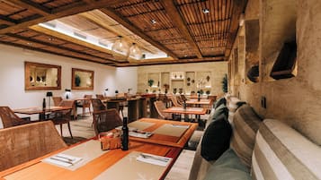 A restaurant with wooden tables and chairs, a sofa, and a high wooden ceiling with skylights.